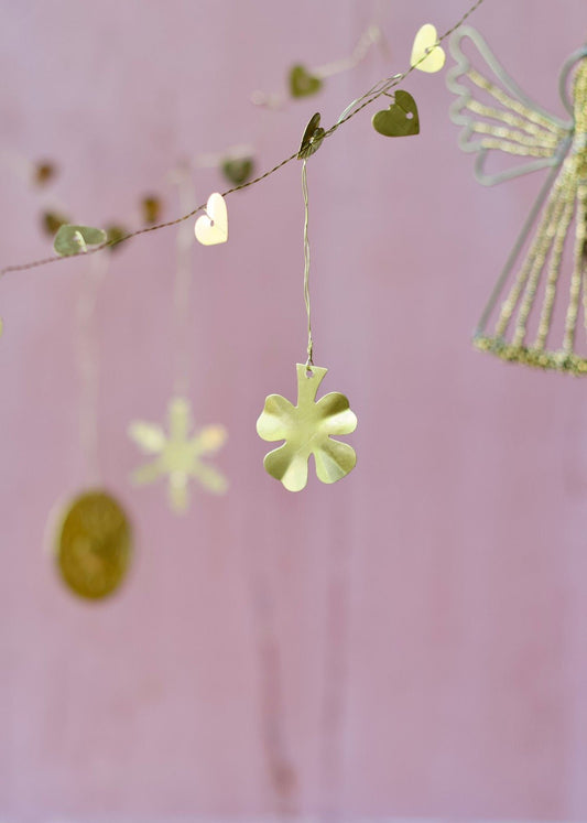 Brass four-leaf clover ornament hanging from a garland with golden hearts against a soft pink background.