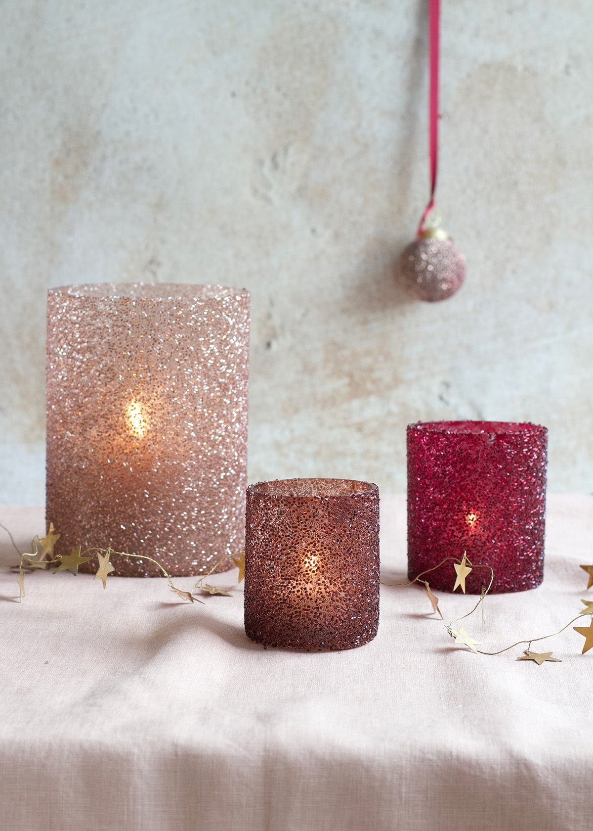 Three glittery candle holders with lit candles on a textured surface.