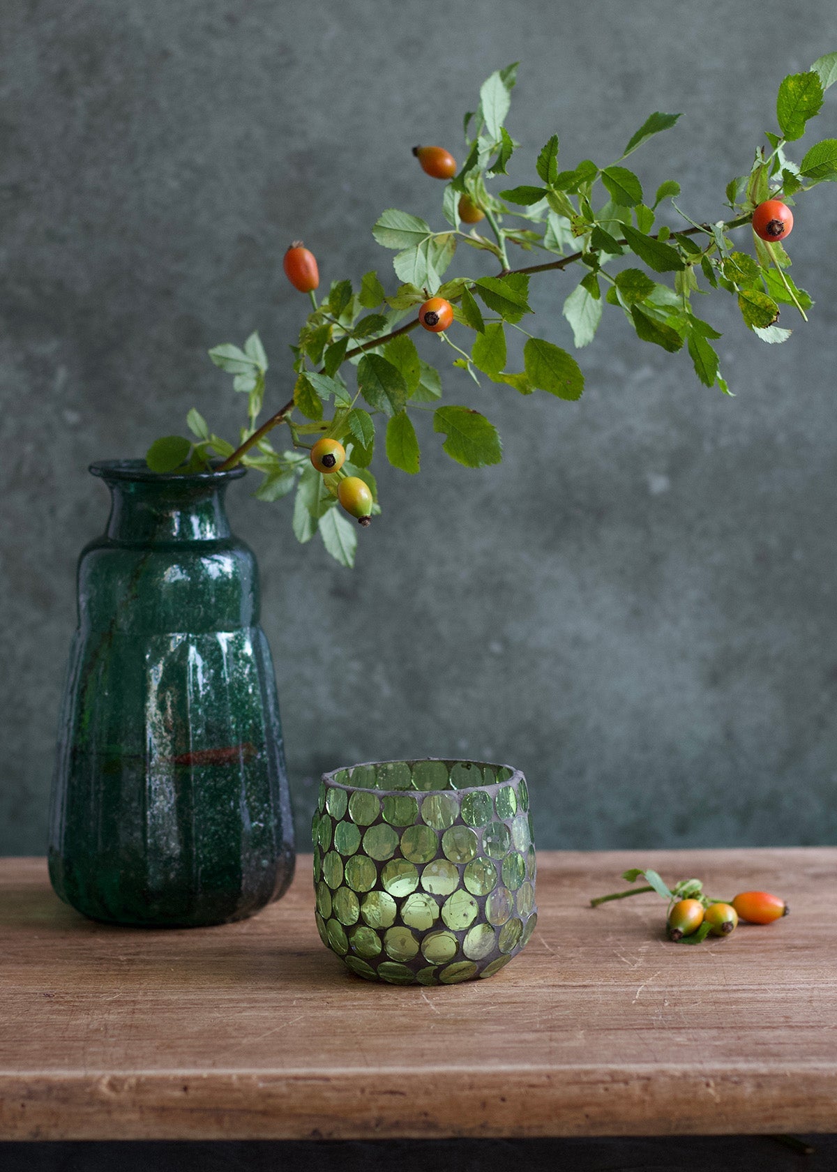Green vase and glass with a branch on a wooden surface