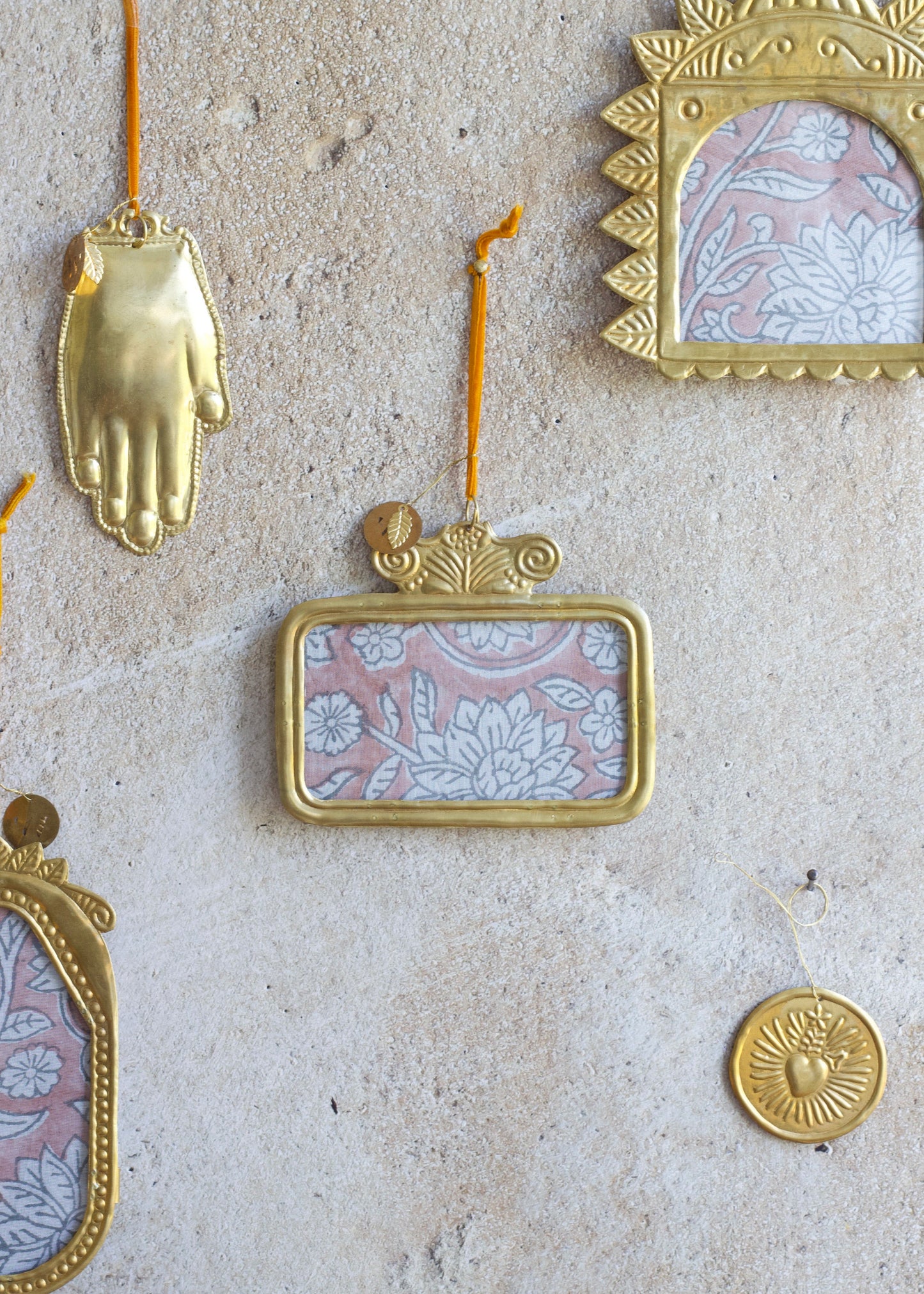 Golden handmade horizontal rectangular ex-voto photo frame with embossed detailing, hanging on a stone wall.