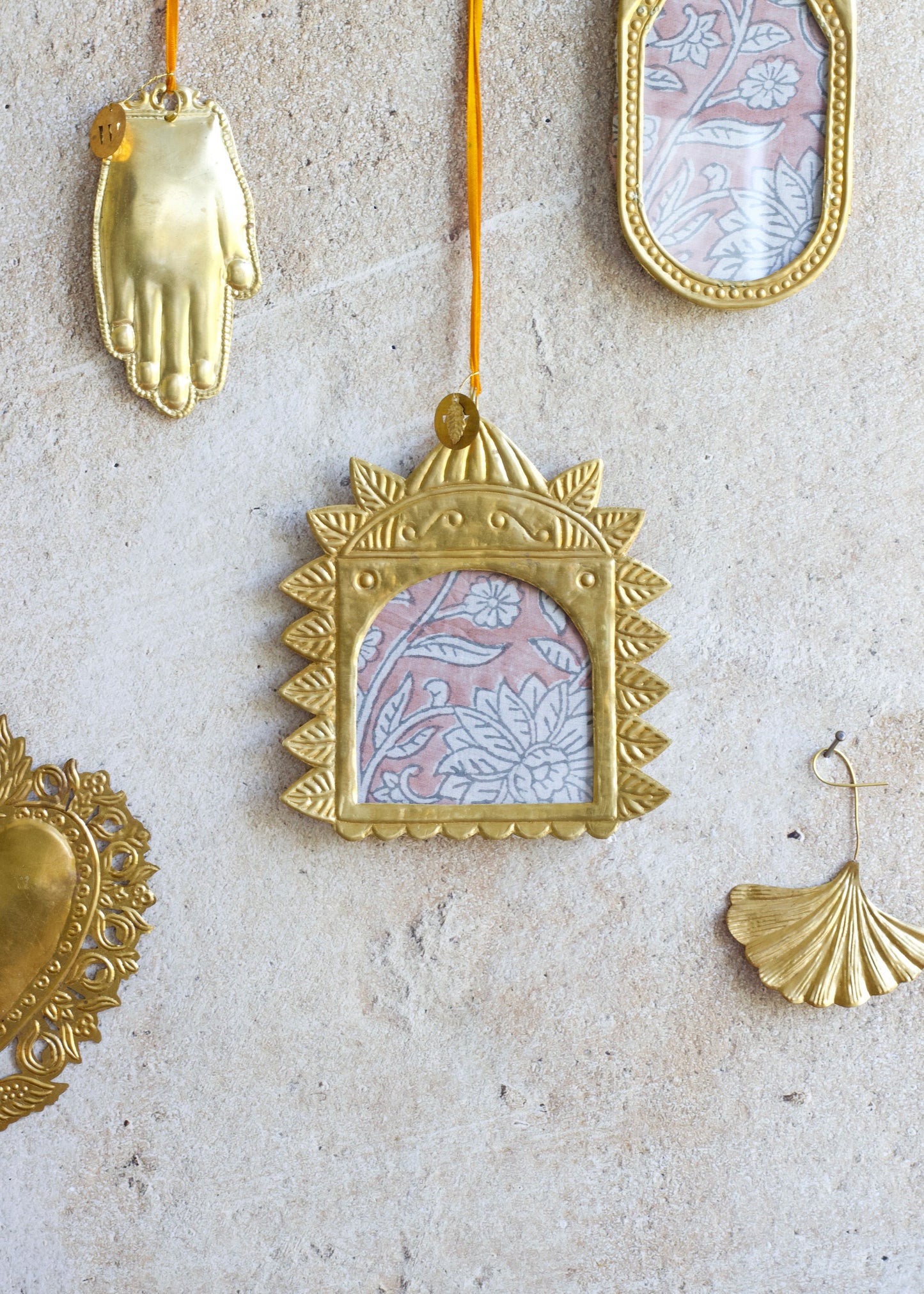 Golden handmade square ex-voto photo frame with embossed sunray border and arched window, hanging on a stone wall.
