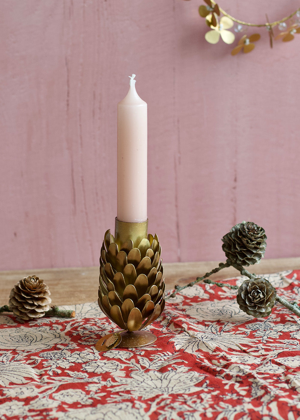 Decorative candle holder with a candle on a tablecloth with pinecones.