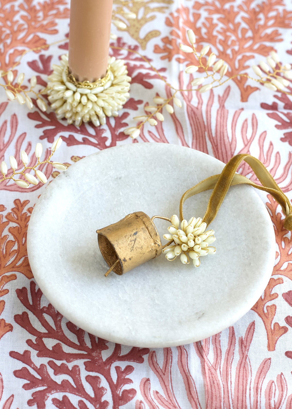 Decorative ring holder with gold and white elements on a coral-patterned background