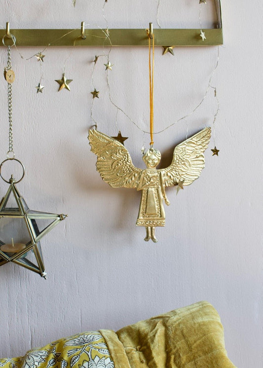 Brass angel ornament with detailed wings hanging from a gold hook, surrounded by star decorations and a glass star-shaped candle holder.