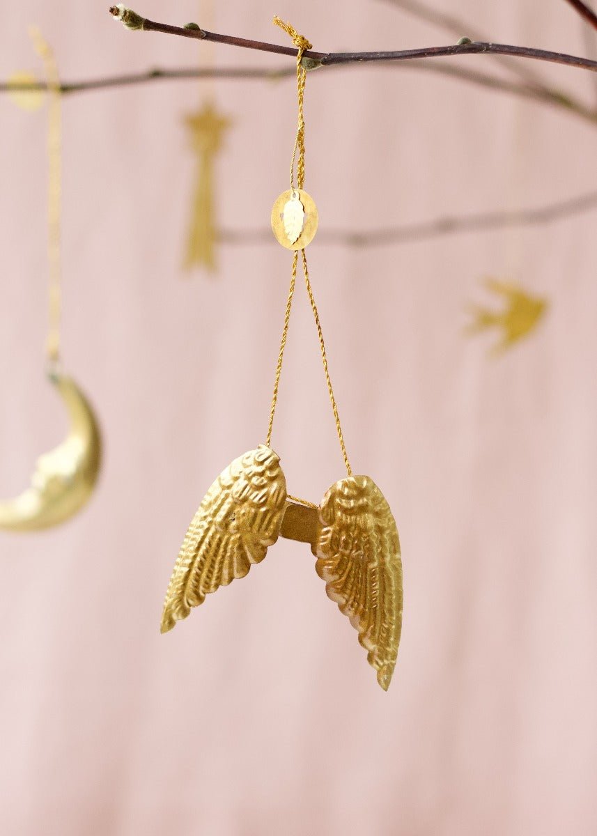 Golden brass angel wings ornament with embossed feather details, hanging from a branch.