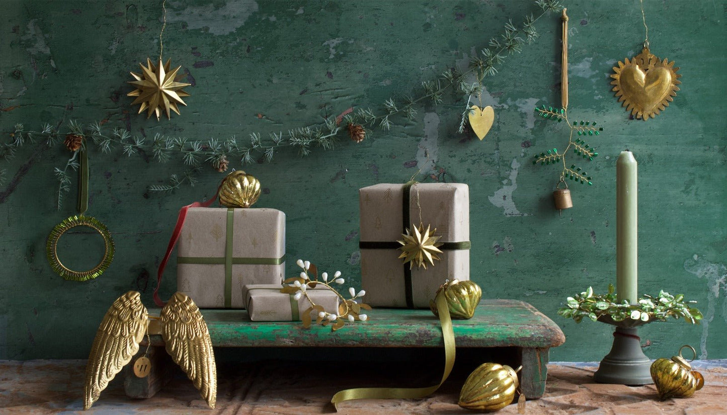 Decorative Christmas setting with golden angel wings, star-shaped ornaments, green candlelight, and beautifully wrapped gifts against a weathered green background.