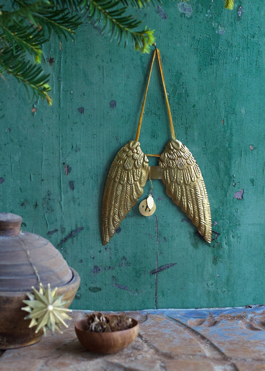 Large gold brass angel wings ornament hanging on green rustic wall with ochre ribbon