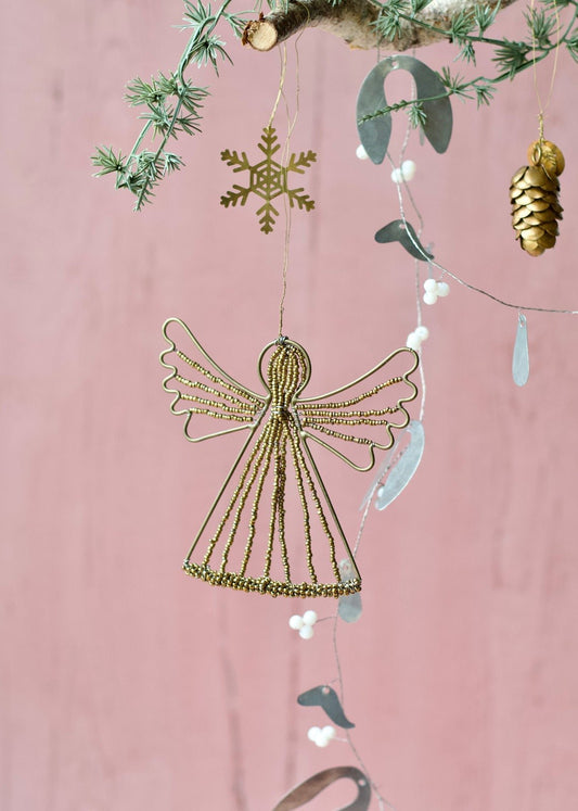 Brass wire angel ornament with golden beads, hanging from a branch against a soft pink background.