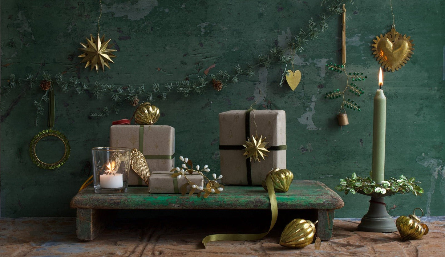 Festive Christmas scene with wrapped gifts, golden ornaments, a green candle in a wreath-shaped holder, a burning tealight, and decorative garlands on a rustic green background.