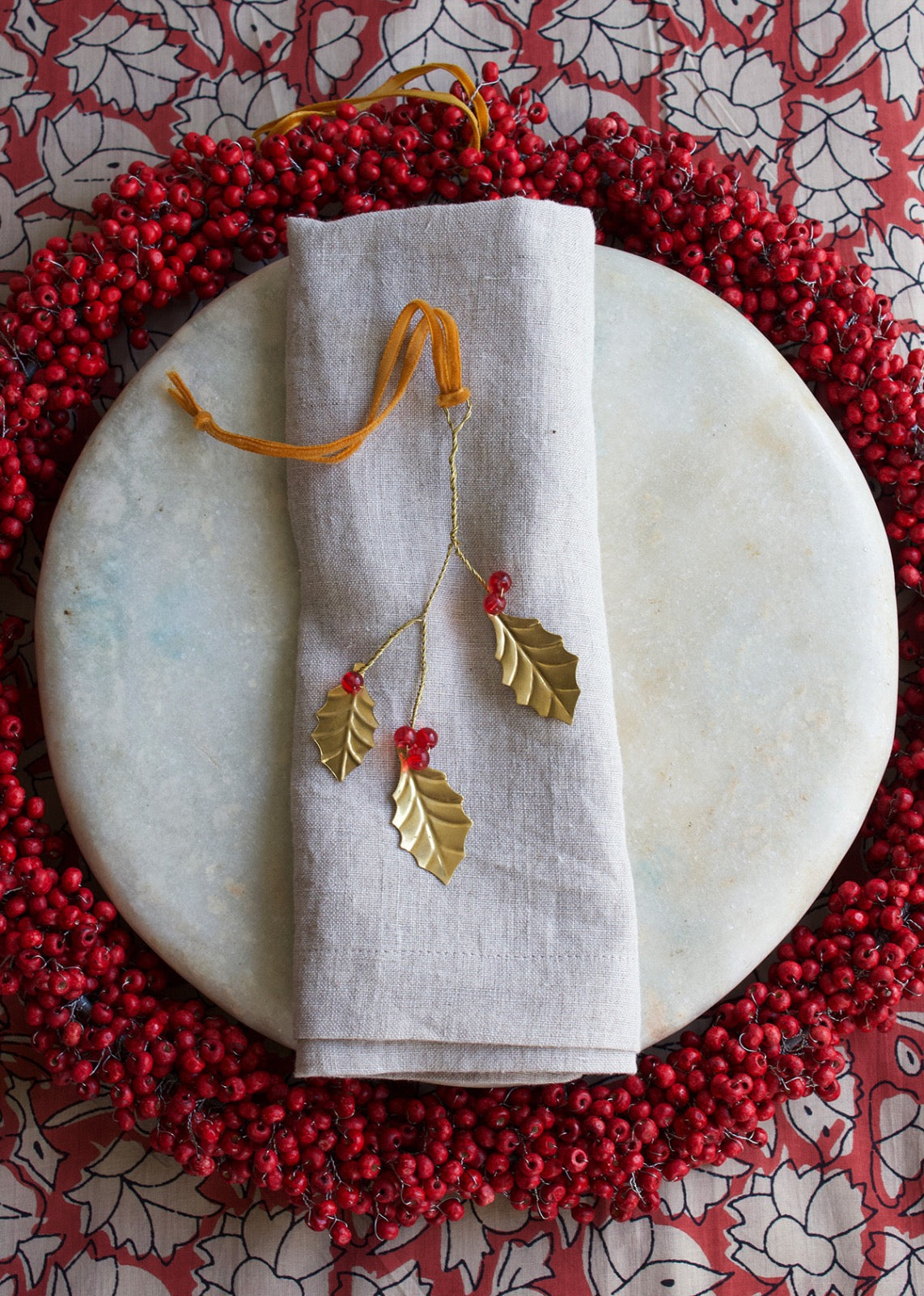 A decorative item with gold-colored branches and red berries, likely a part of holiday decor, displayed on a white surface with a red and white patterned background.
