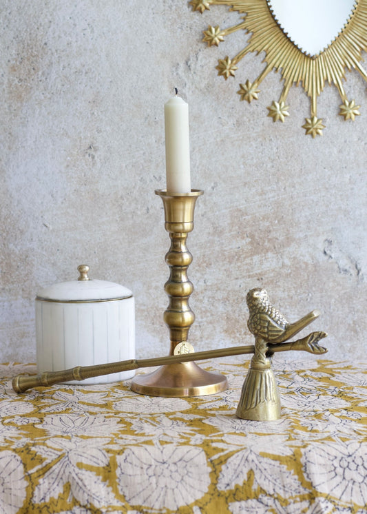Decorative items including a gold candlestick, bird-shaped holder, and white container on a textured surface.