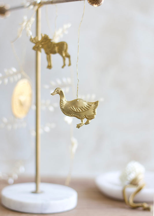 Brass duck ornament hanging from a wire, with soft background elements and blurred animal shapes.