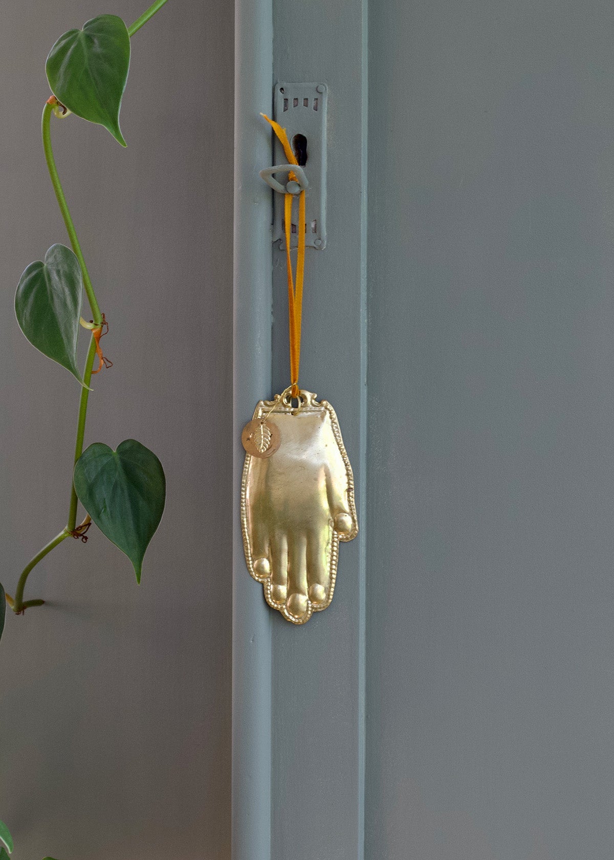 Gold hand-shaped ornament hanging on a light blue door with green leaves in the background