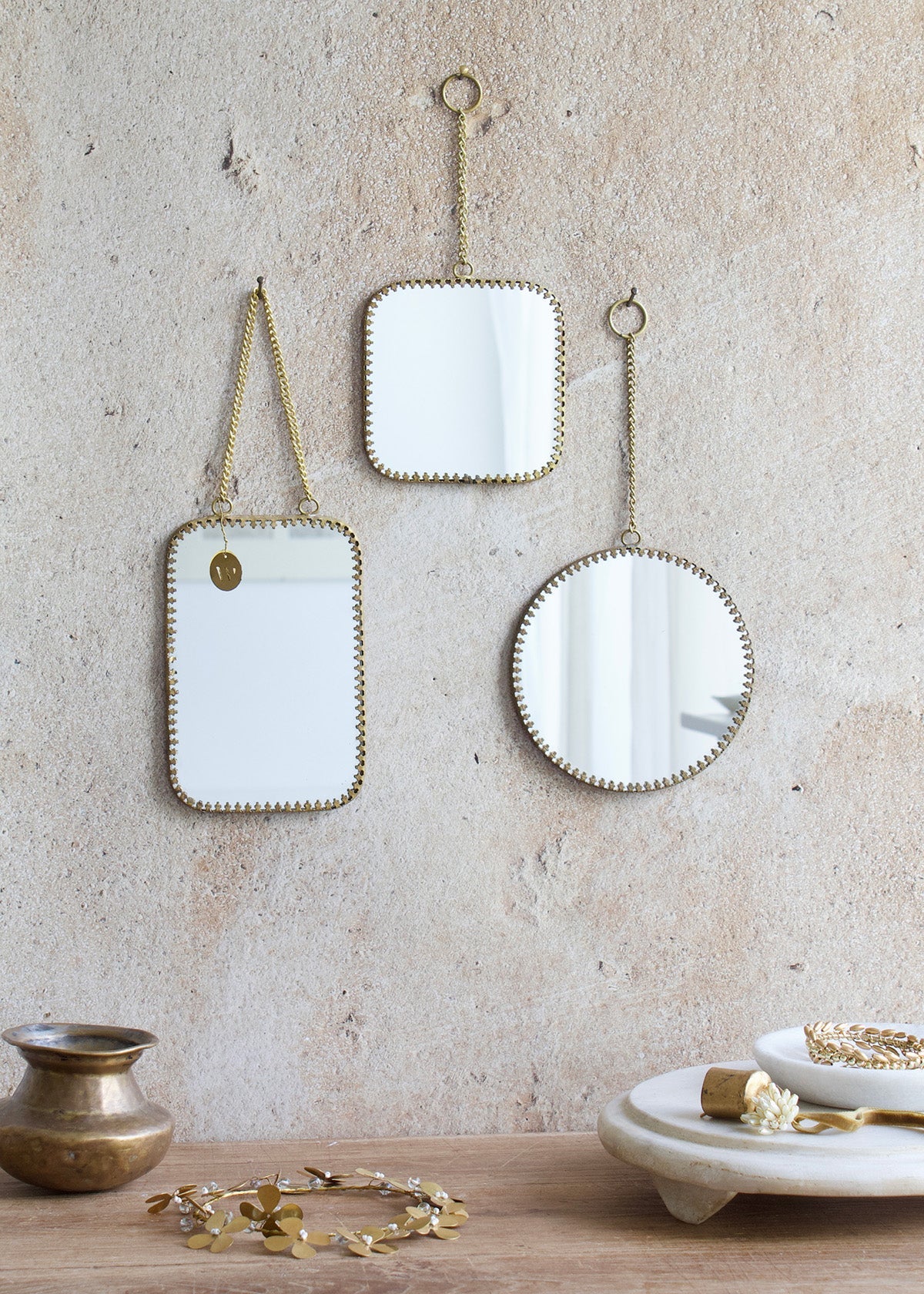 Three decorative mirrors hanging on a textured wall with a wooden surface below.