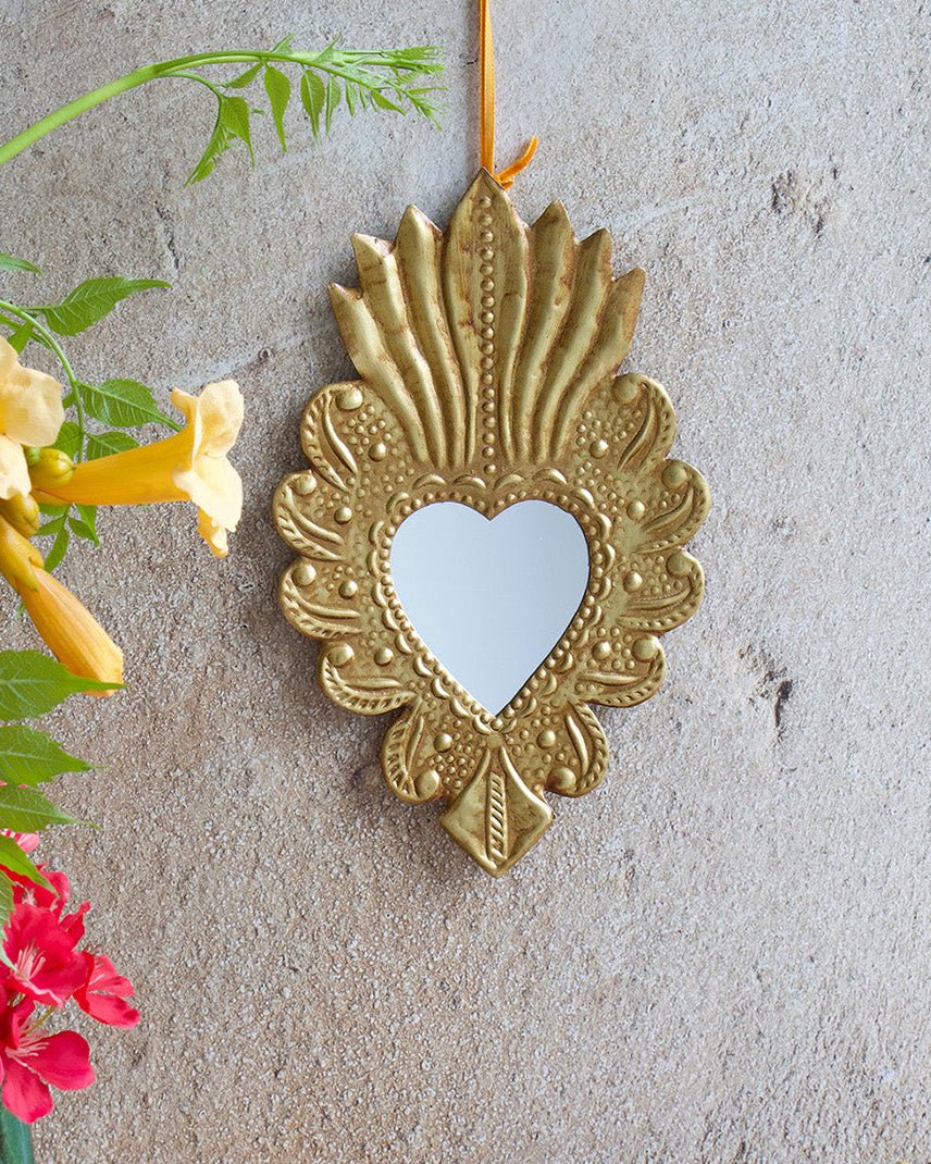 Decorative gold heart-shaped mirror on a textured wall with flowers and fabric in the foreground.