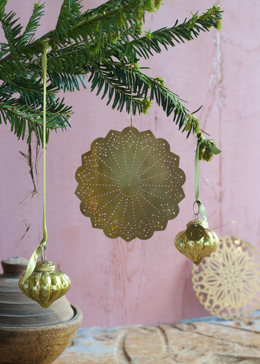 Golden brass mandala ornament with delicate cut-out details, hanging on a fir branch.