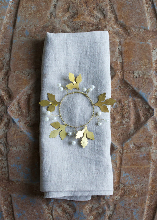 Brass napkin ring with golden leaves and white pearls on a linen napkin.