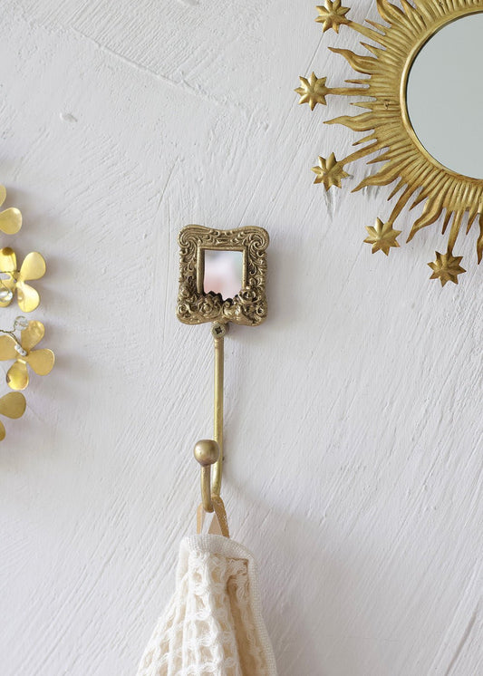 Decorative gold hook with a small mirror on a white wall.