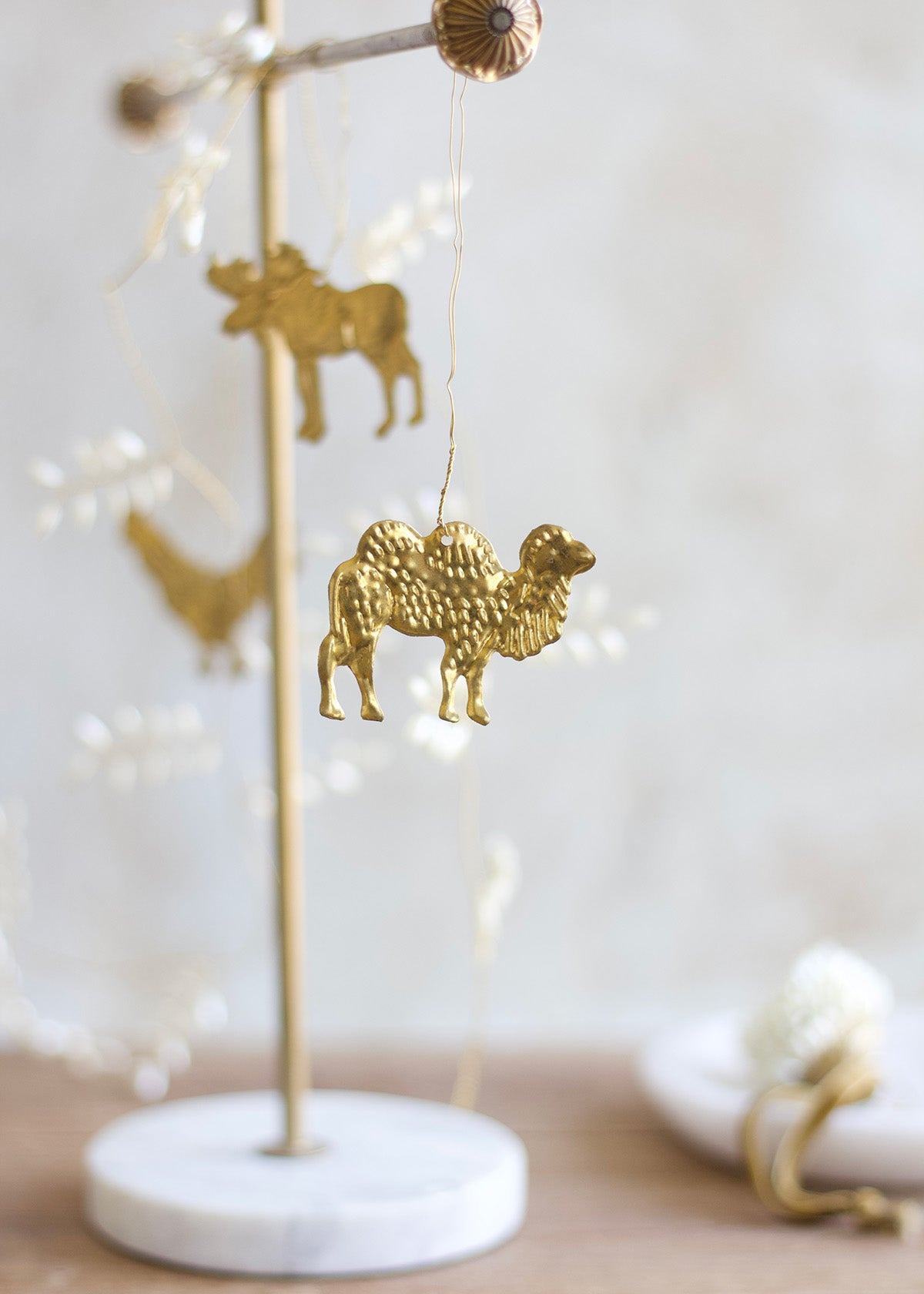 Brass camel ornament hanging from a decorative wire garland with a marble stand and softly blurred background.