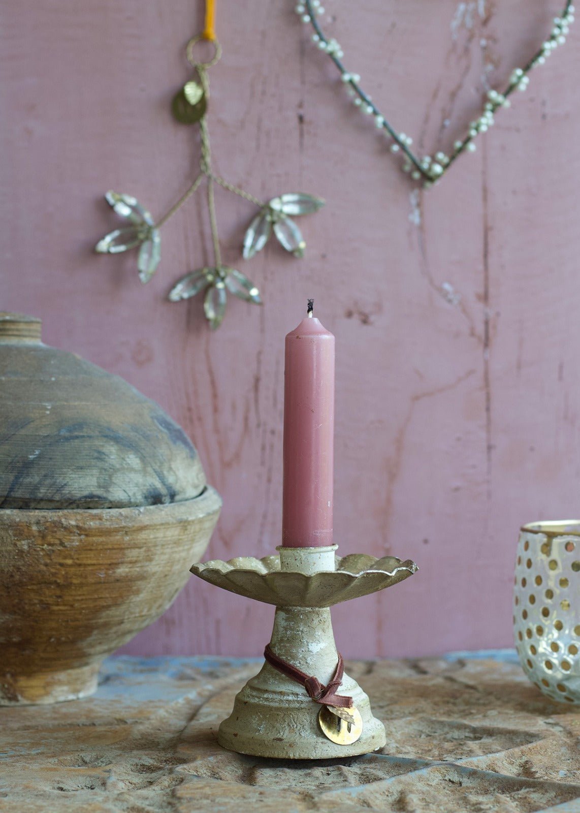 Pink candle on a decorative holder with a pink wall and hanging decorations in the background