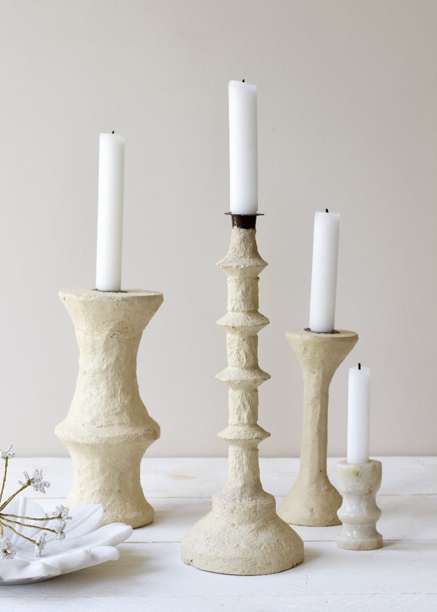 Set of paper mache candle holders with white candles on a neutral background
