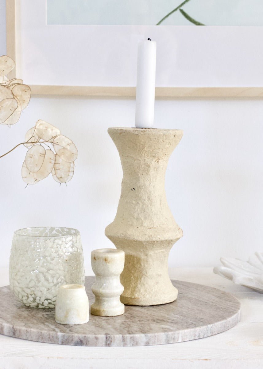 Decorative candle holders on a round wooden tray with a white candle.
