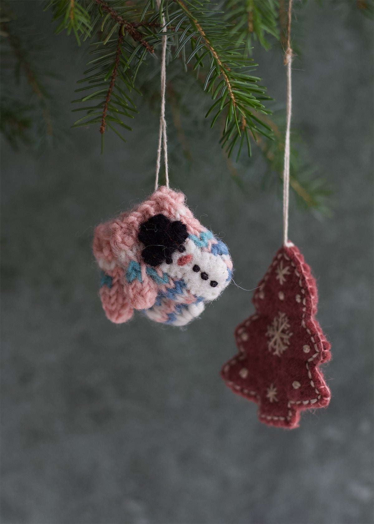 Small pink and multicolor felt mug ornament with black flower detail, hanging from a Christmas tree branch.