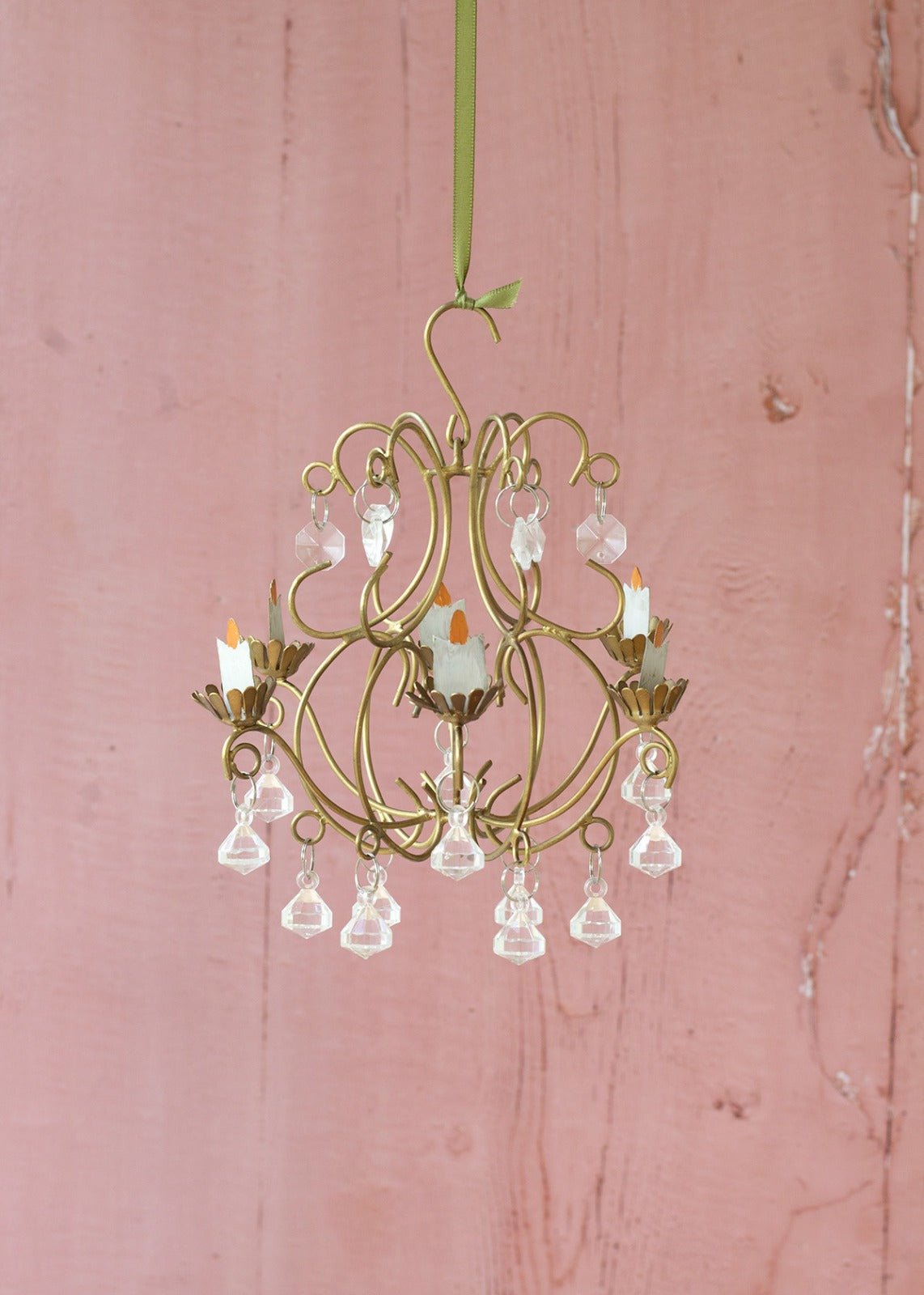 Small gold chandelier with crystal accents on a pink wooden background
