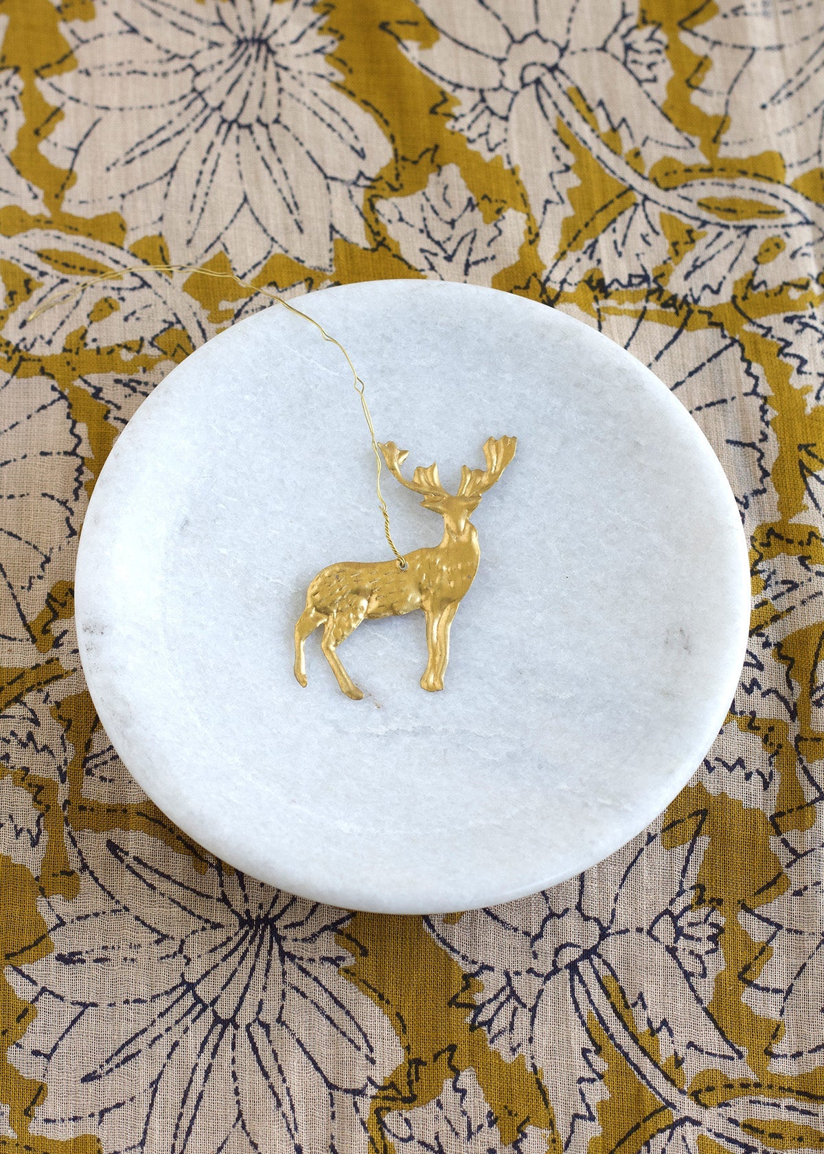 Gold deer pendant on a white marble coaster with a floral patterned fabric background