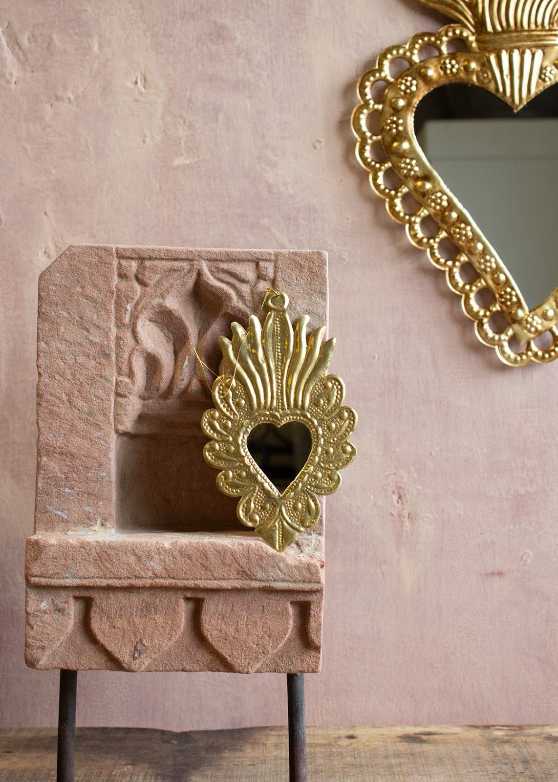 Decorative gold heart-shaped mirror on a stone surface with a pink wall background