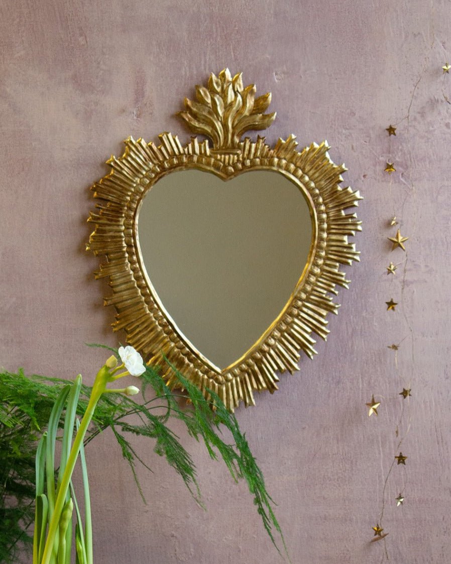 Heart-shaped gold mirror on a pink wall with decorative elements