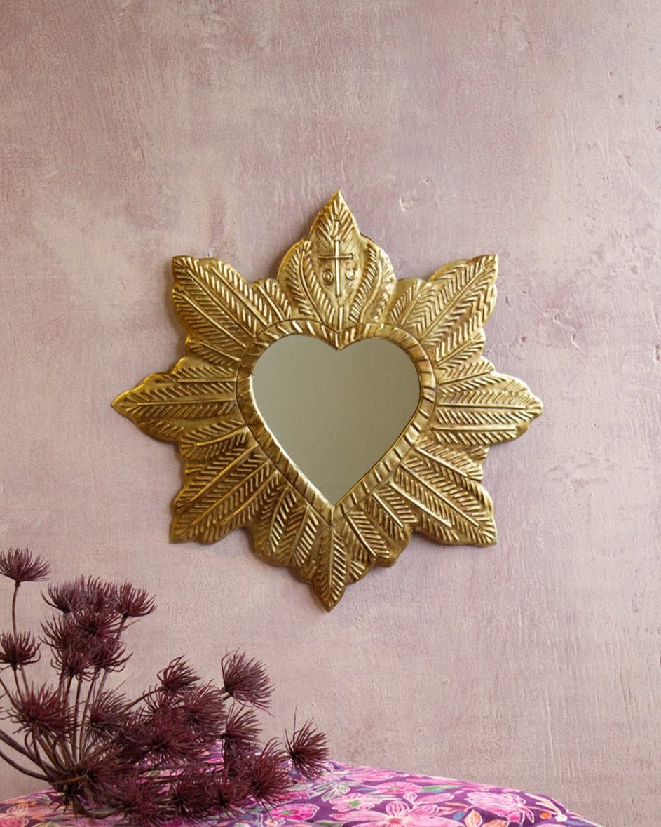 Decorative gold mirror with heart-shaped center on a textured wall above a floral-patterned fabric.