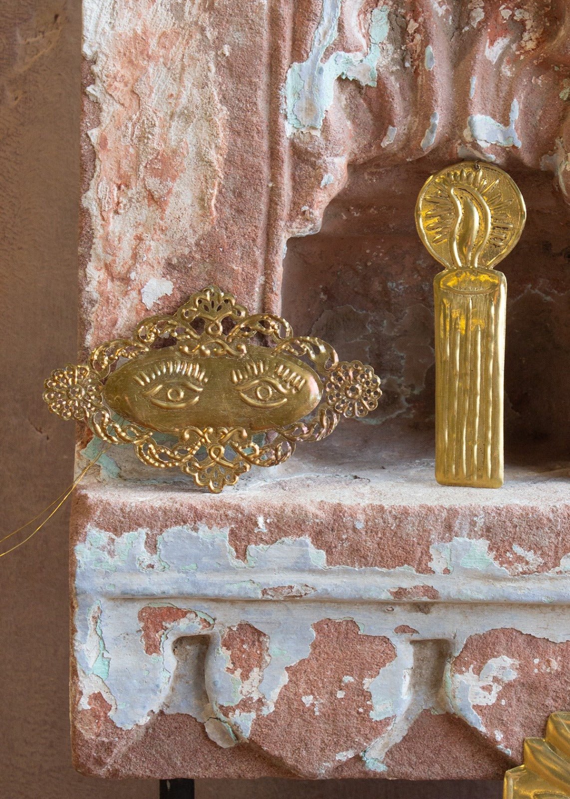 A decorative brass pendant featuring two eyes, placed on a textured surface with a reflective gold finish.