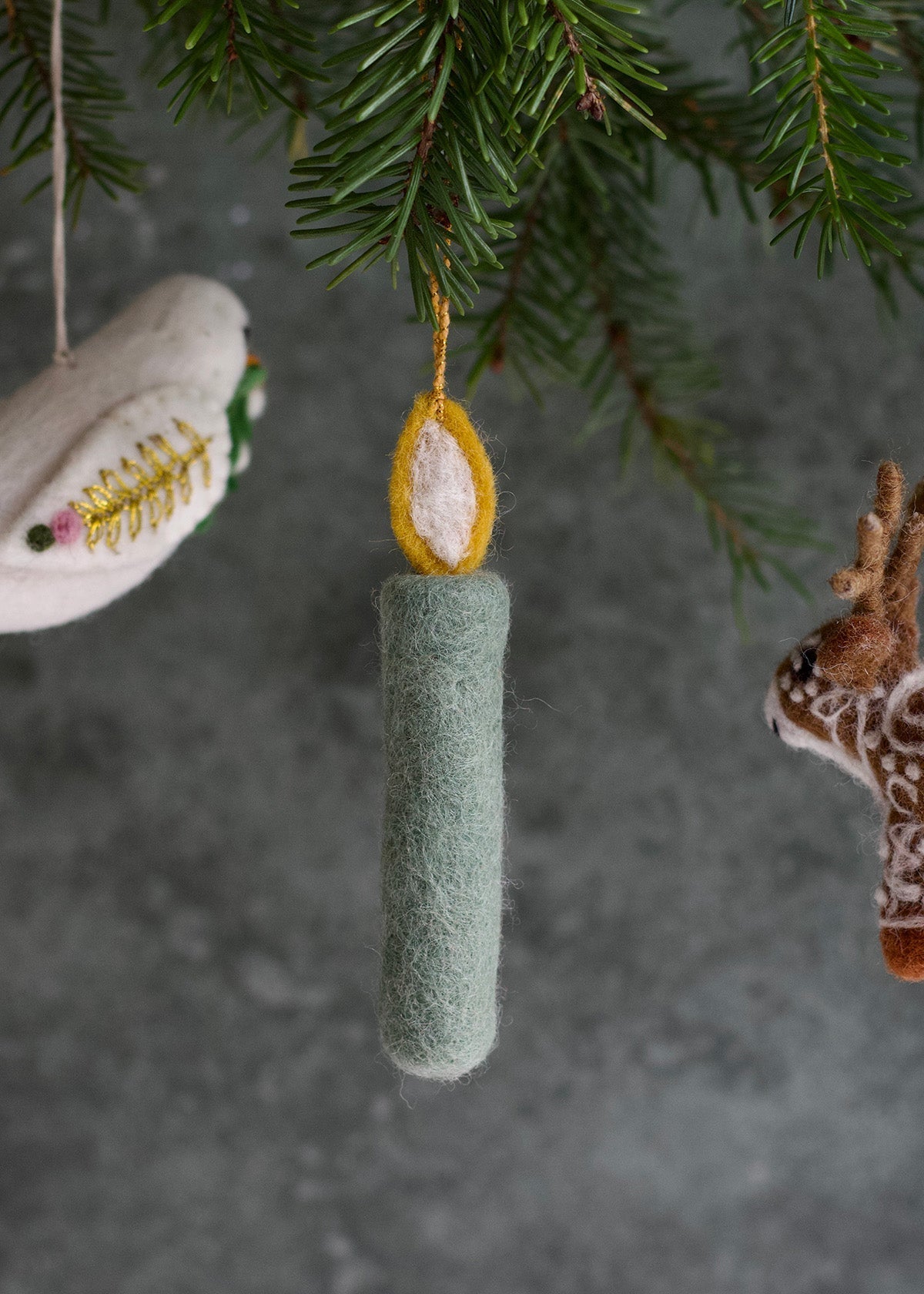 Green cylindrical ornament hanging from a tree branch with other ornaments.