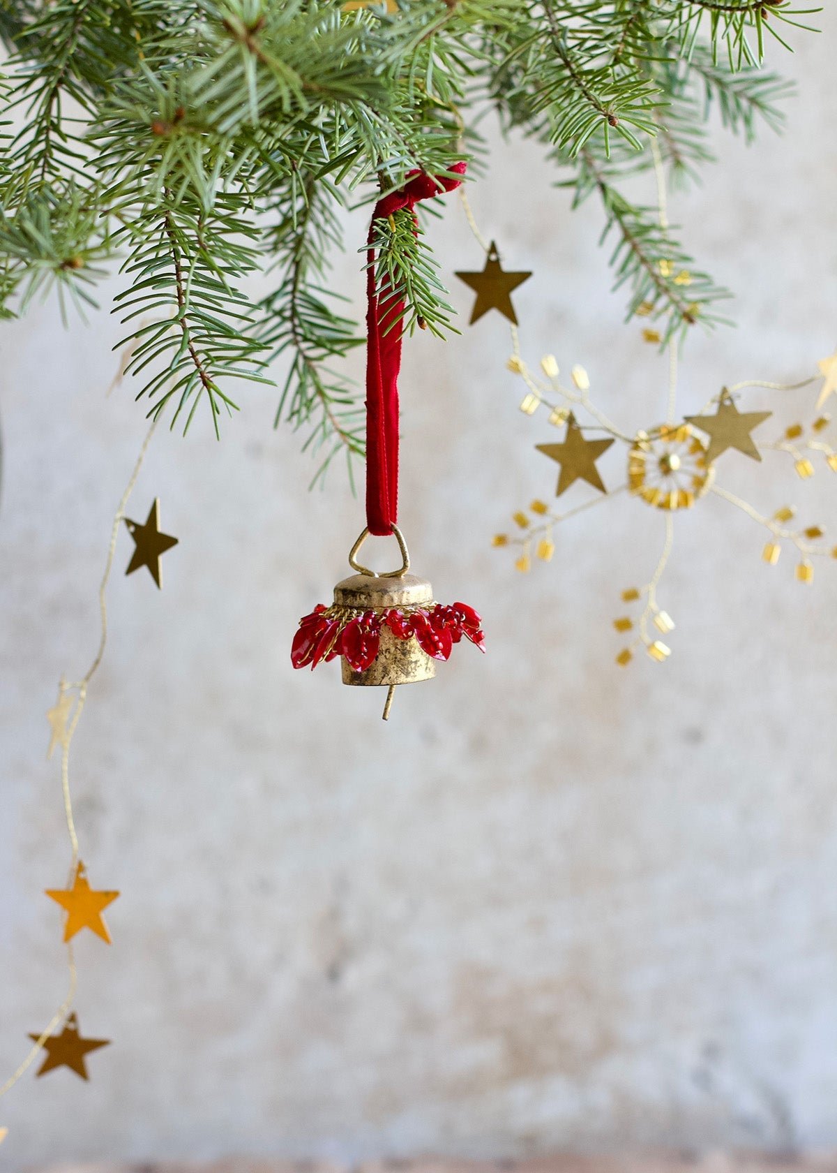 Decorative Christmas bell ornament with red berries hanging on a branch with gold stars and string lights in the background.