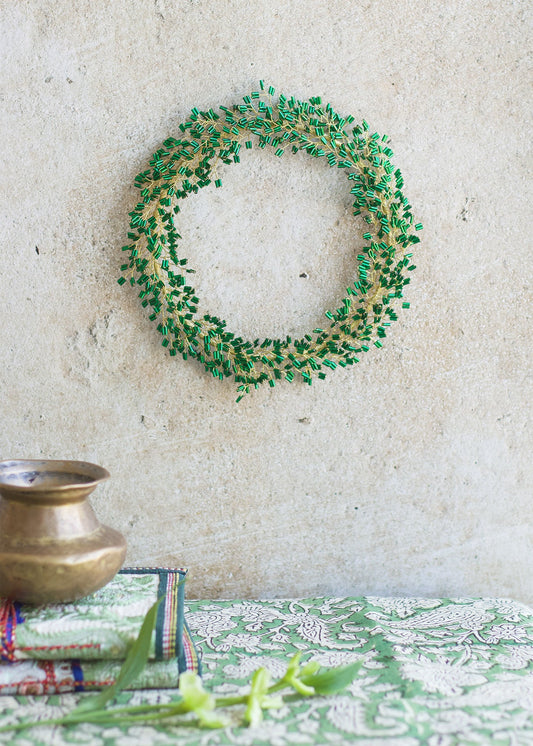 Green wreath on a textured wall with a decorative tablecloth and pot below.