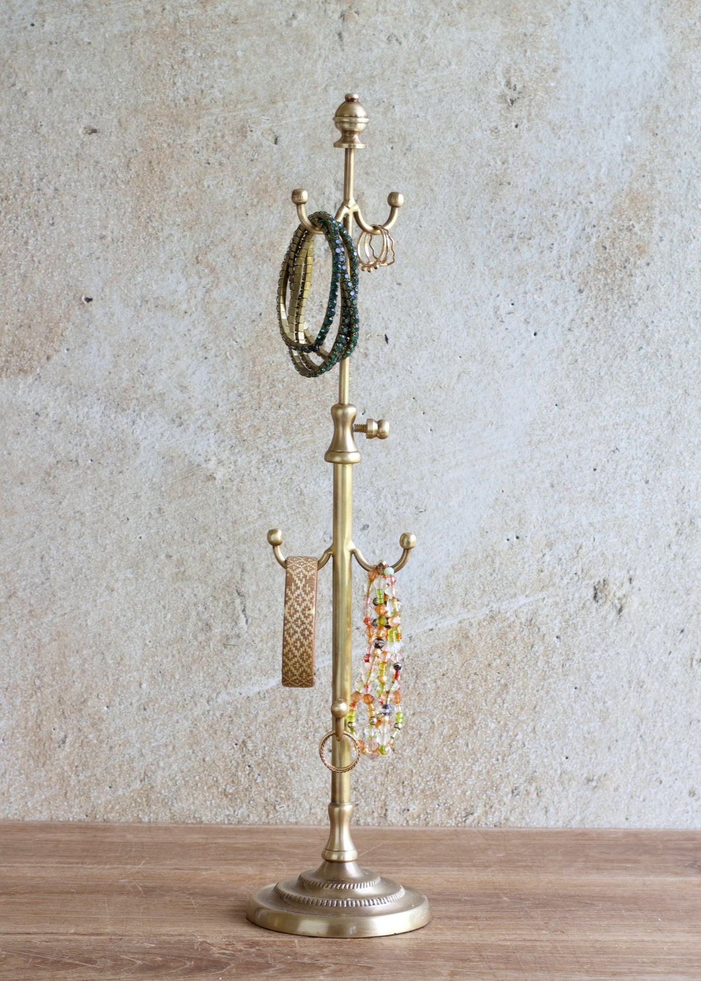 Brass jewelry stand with bracelets on a wooden surface and textured wall background