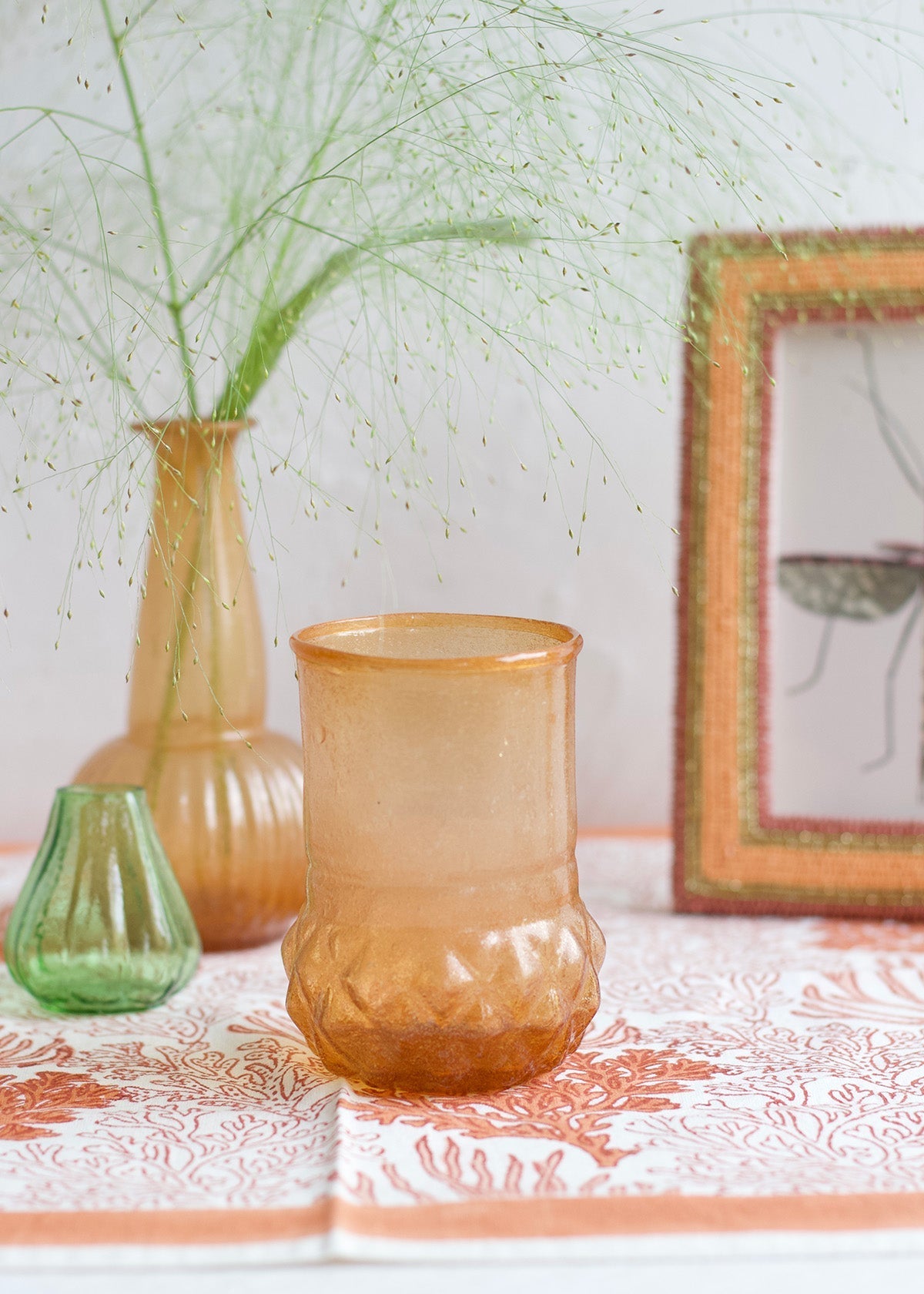 Three glass vases on a table with a framed picture in the background