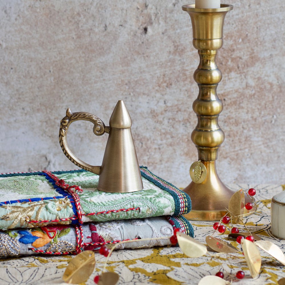 Decorative setting with a brass candlestick holder, decorative pitcher, and colorful fabric on a textured surface.