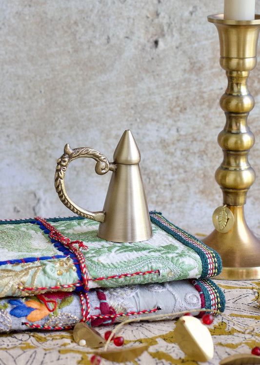 Decorative stack of fabric with a brass teapot and candlestick on a textured surface.