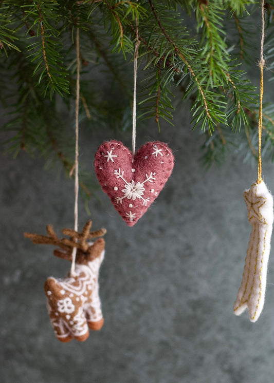 Heart-shaped ornament with floral patterns hanging from a branch against a textured gray background