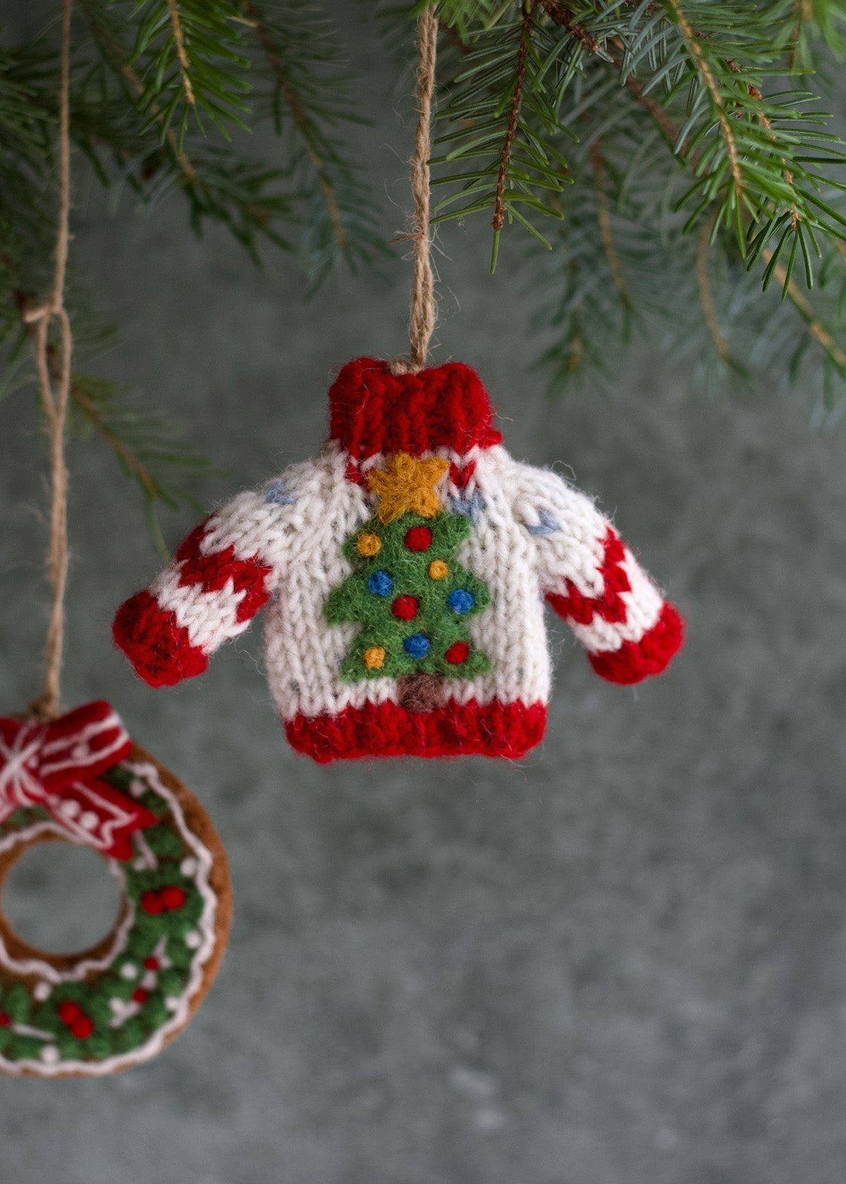 Knitted Christmas sweater ornament hanging on a tree branch with a green background