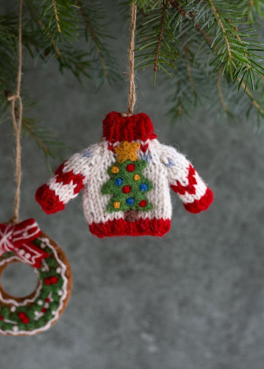 Knitted Christmas sweater ornament hanging on a tree branch with a green background