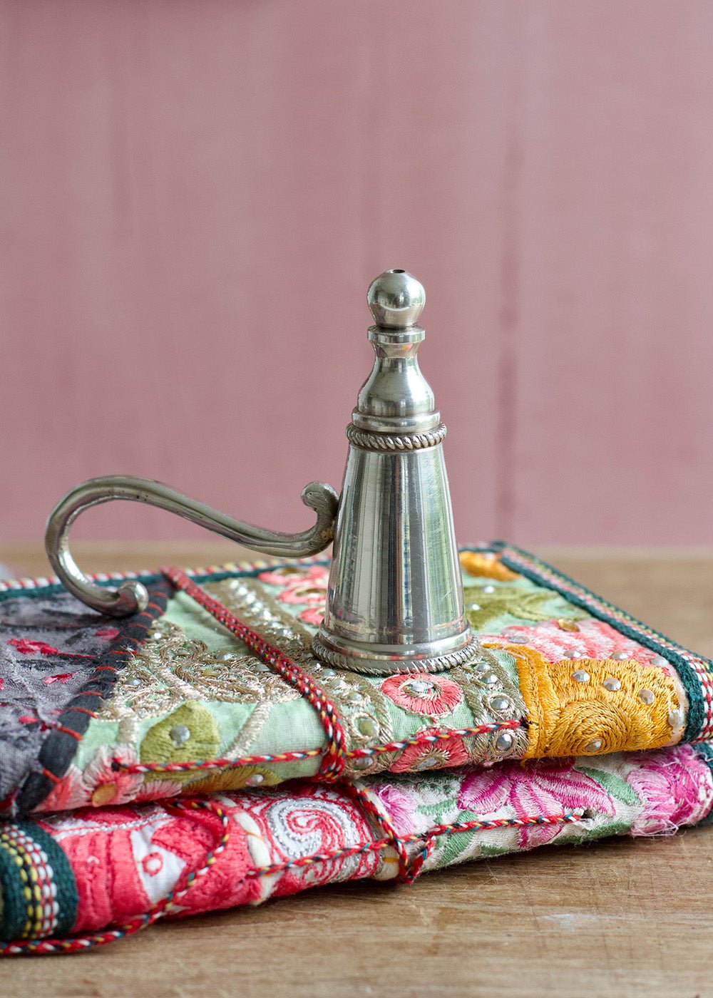 Decorative stack of fabric-covered books with a metallic object on top against a pink background