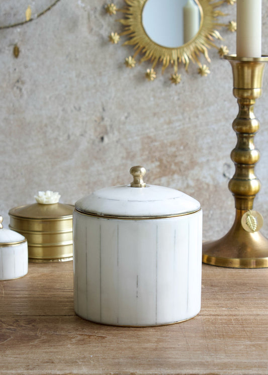 Decorative ceramic jar with gold accents on a wooden surface, with a gold candlestick and mirror in the background.