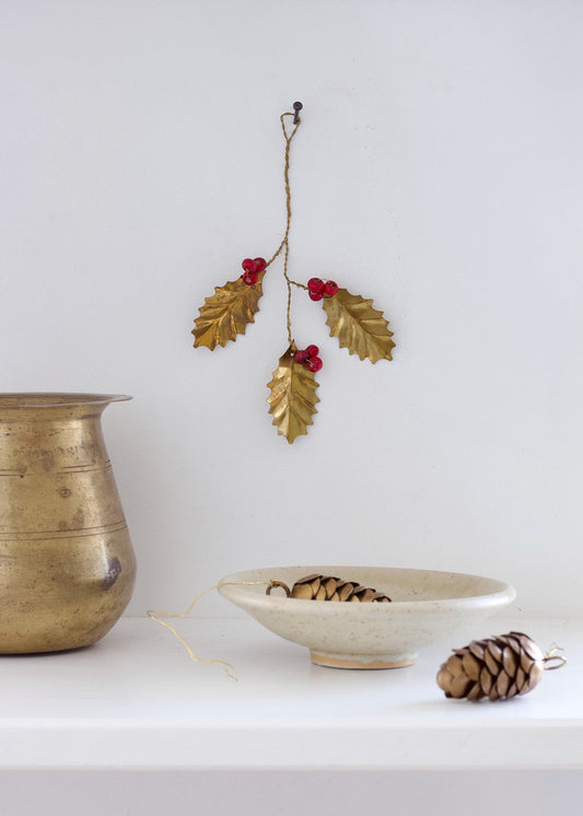 Decorative gold leaf and berry branch with a ceramic bowl and pinecones on a white surface.