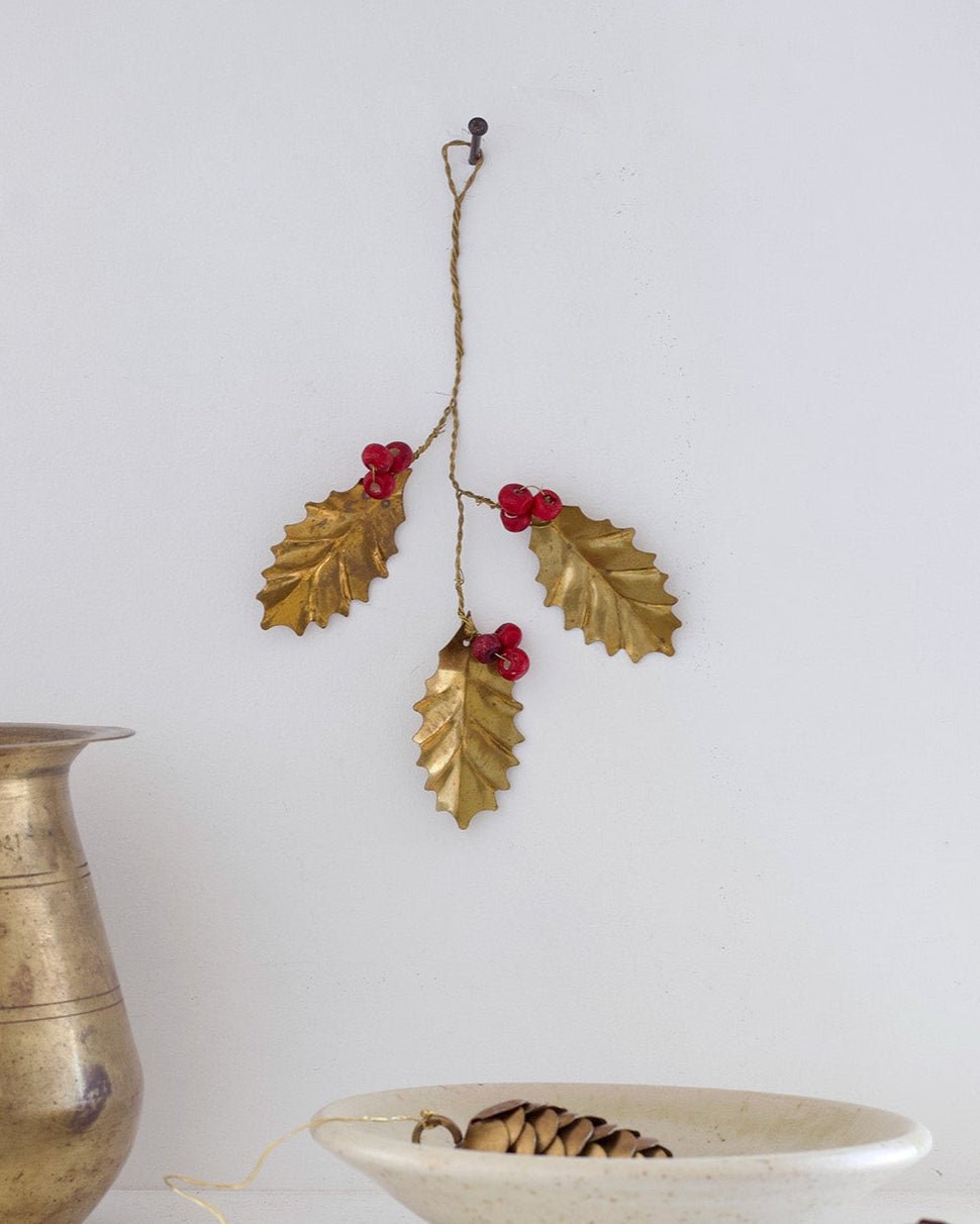Decorative gold leaf and berry branch with a ceramic bowl and pinecones on a white surface.