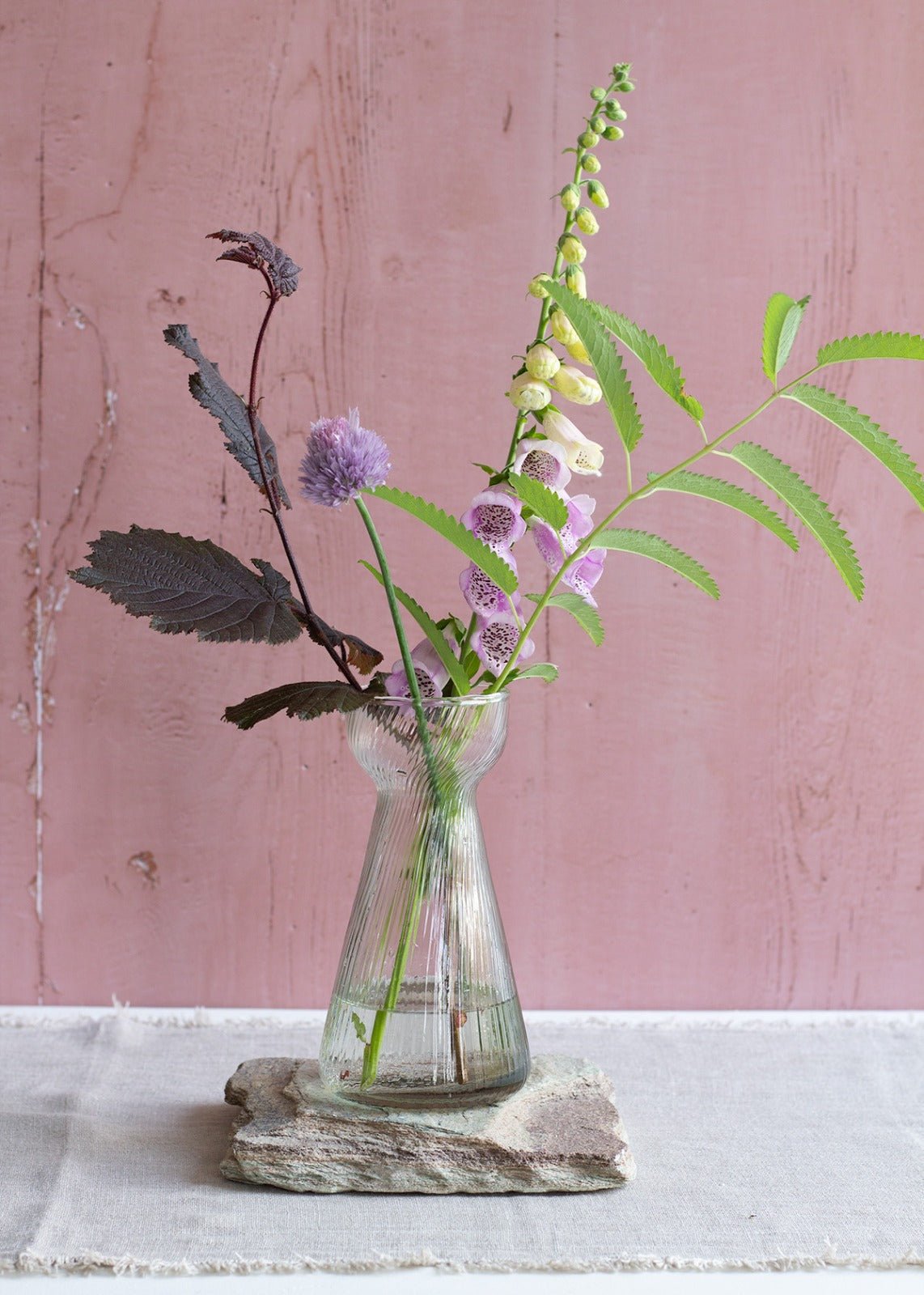 Slim ribbed glass vase with a narrow waist, holding wildflowers against a blush pink background.