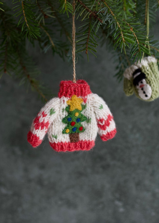 Knitted Christmas sweater ornament with a tree design hanging on a tree branch.