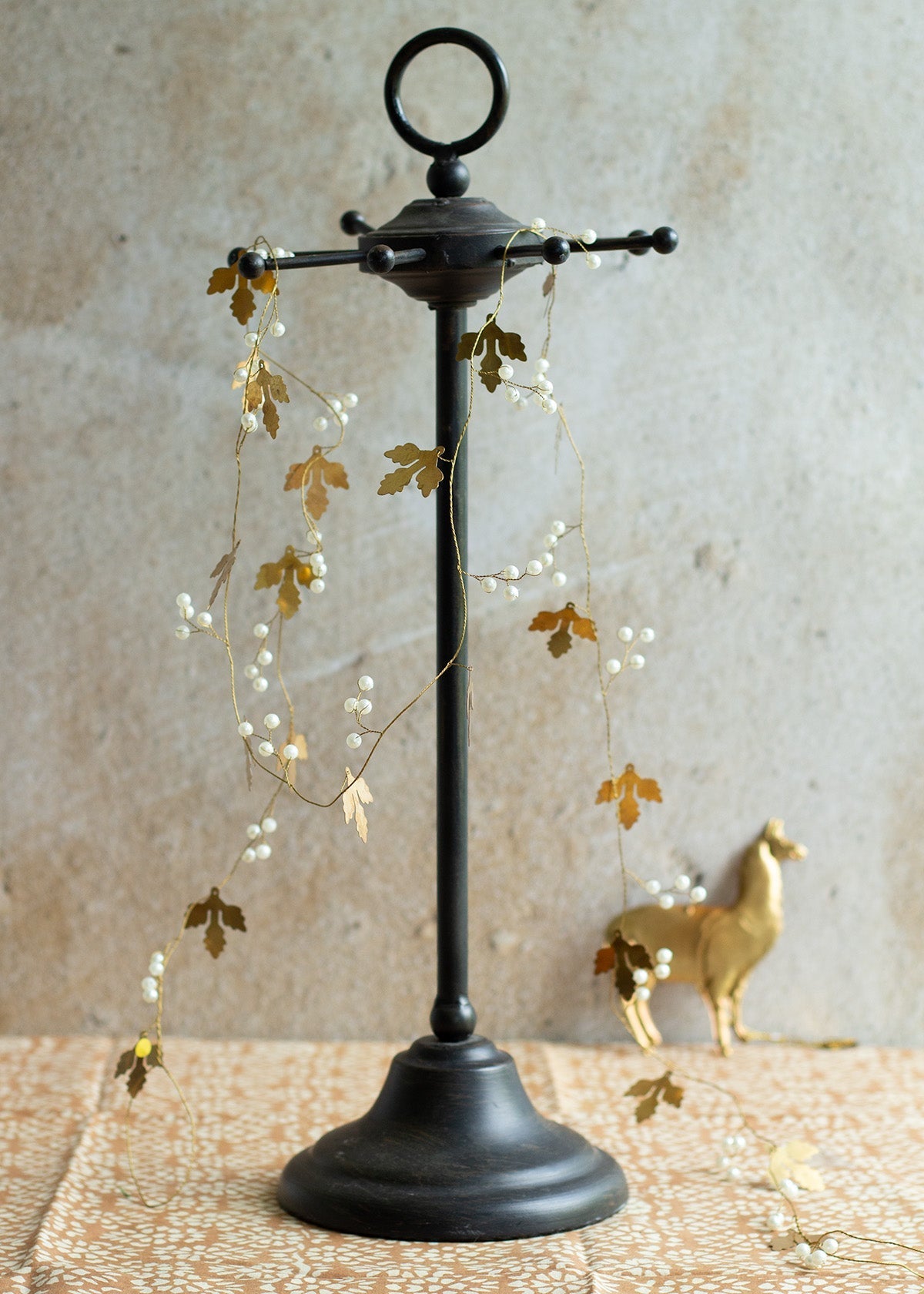 Black metal stand with gold leaf and pearl garland draped over it, brass llama in background
